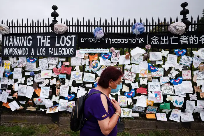 Woman passes a fence outside Brooklyn's Green-Wood Cemetery adorned with tributes to victims of COVID-19, in New York on May 28th, 2020.